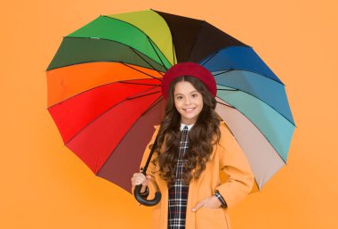 Yağmurlu gün eğlencesi. Şemsiye altında iyi yürüyüşler. Yağmur konseptinin tadını çıkar Çocuk mutlu bir şekilde renkli gökkuşağı şemsiyesi tutuyor. Yağmurlu hava ve uygun giysiler. Parlak şemsiye. Eğlenmene bak. Pozitif olma kavramı.
