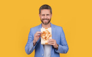 cheerful guy hold gift box isolated on yellow background. guy hold gift box in studio. guy with gift box for holiday. photo of guy holding occasion gift box.