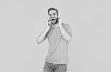 Mavi gömlekli neşeli adam sarı arka planda kulaklık takıyor..