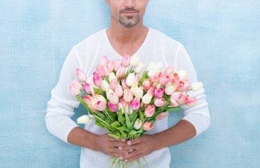 cropped view of man with spring tulips isolated on blue background. photo of man with spring tulips. man with spring tulips. man with spring tulips in studio.