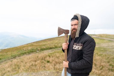 bearded man lumberjack hold axe outdoor, advertisement. bearded man lumberjack has axe. bearded man lumberjack with axe. photo of bearded man lumberjack holding axe in the mountain.