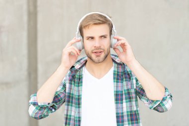 concentrated man listening music and wearing checkered shirt. photo of man listening music in headphones. man listening music outdoor. man listening music outside.