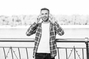 Tıraşsız, mutlu, yakışıklı, kareli gömlekli adam kulaklıkla müzik dinliyor, açık havada müzik dinliyor..