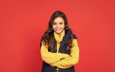 Kış mevsiminde kıvırcık saçlı mutlu çocuk kırmızı arka planda yelek, saç bakımı.