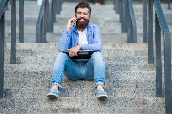 photo of guy talk on smartphone sit on stairs. guy talk on smartphone outdoor. guy talk on smartphone outside. guy talk on smartphone in the street.
