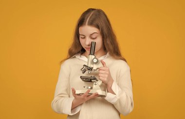 Sarı arka planda mikroskobu olan ciddi bir çocuk.