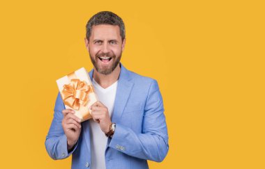 photo of surprised guy holding occasion gift box. guy hold gift box isolated on yellow background. guy hold gift box in studio. guy with gift box for holiday.