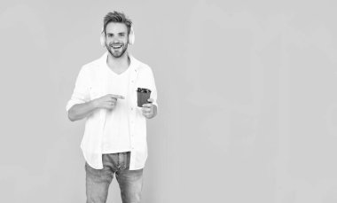 Müzik dinle. Kablosuz cihaz aksesuarı. Yeni teknoloji. Kulaklıklı mutlu adam kahve fincanını işaret ediyor. Online eğitim. Okula dönüyorum. Kulaklıklı genç adam kahve içer. Müzik aşığı.