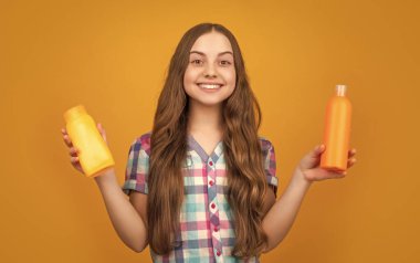 Sarı arka planda şampuan şişesi olan gülümseyen çocuk..