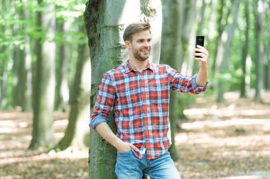 cheerful man blogger take selfie on phone. man blogger take selfie on smartphone. photo of man blogger take selfie in the forest. man blogger take selfie outdoor.