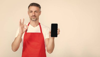 Önlüklü neşeli olgun bir adam akıllı telefona fotokopi alanı sunuyor. Tamam.