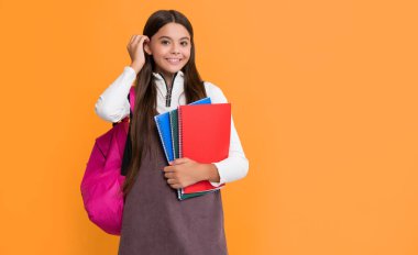 Okul çantası ve sarı arka planda not defteri olan mutlu bir çocuk..