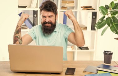 Ofis masasına dizüstü bilgisayara bakarak kazanma jesti yapan heyecanlı adam, iş başarısı.