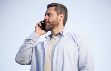 Telefonda erkek erkeğe konuşma. Adam akıllı telefondan konuşuyor. Gökyüzü arka planında insan iletişimi.