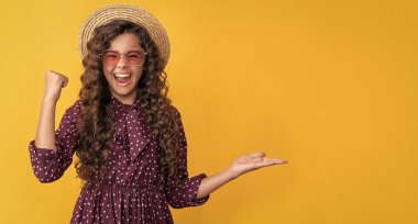 Hasır şapkalı, güneş gözlüklü, uzun kıvırcık saçlı gülümseyen bir çocuk. Boşluğu kopyala.