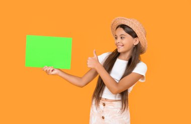 Sarı arka planda yeşil kağıt üzerinde fotokopi alanı olan neşeli genç kız. başparmak yukarı.