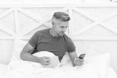 Mutlu adam sabah kahvesi ve sms ile yatakta dinlenirken cep telefonu kullanıyor..