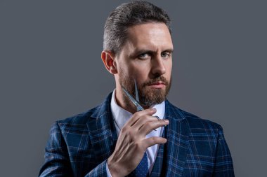 face of barber man hold scissors isolated on grey background. barber man with scissors. man with scissors in barber studio. photo of bearded man with barber scissors.