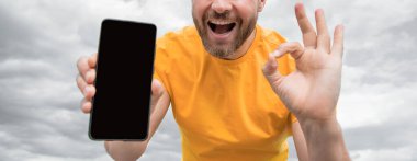 Akıllı telefon ekranı ile fotokopi alanı sunan adamın kırpılmış görüntüsü. Tamam jest gösteriliyor.