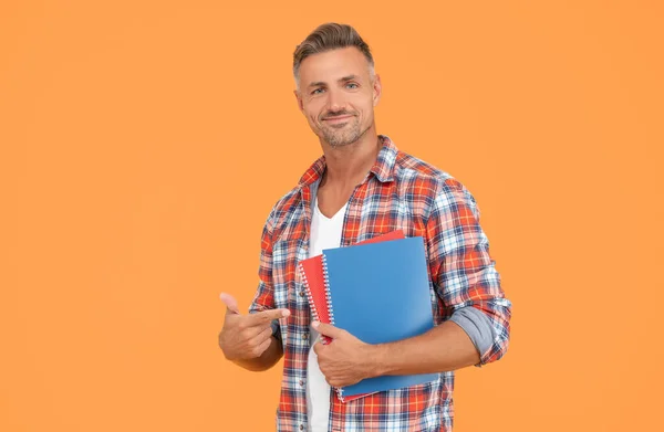 Happy man student pointing finger at books yellow background, education.