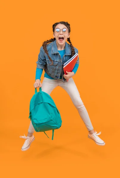 Excited girl jumping after school yellow background. Energetic teenager screaming in midair, school. Back to school.