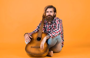 Yakışıklı müzisyen gitarist. Otururken gitar çalan karizmatik olgun bir adam. En sevdiğin müzikle rahatla. Gitarlı adam şarkı söylüyor. Sarı zemin üzerinde gitarist.