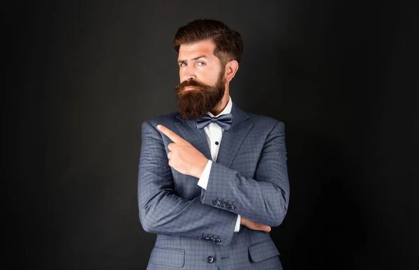 serious man in tuxedo bow tie. bride groom in formalwear pointing finger on black background. male formal fashion. copy space.