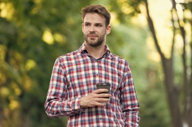 Genç adam damalı gömlekle kahve fincanı ile gülümsüyor..