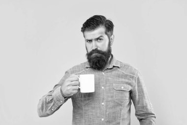 Elinde çay fincanı olan ciddi bir beyaz adam. Sarı arka plan..