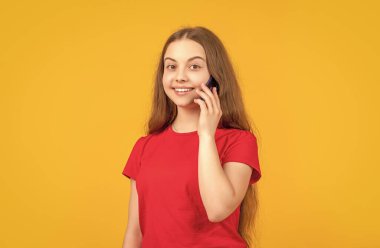 Sarı arka planda akıllı telefonu olan neşeli bir kız..