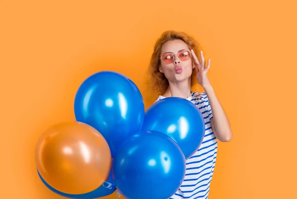 party girl with balloon in sunglasses. girl blow kiss hold party balloons in studio. girl with balloon for party isolated on yellow background.