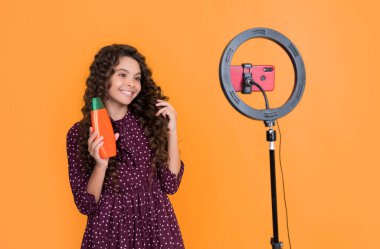 Uzun kıvırcık saçlı mutlu çocuk blog şampuanı için video yapıyor..