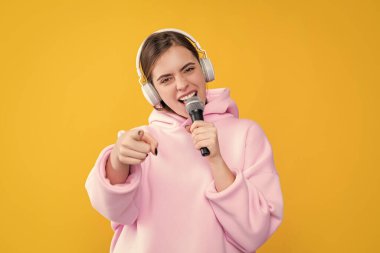 Sarı arka planda mikrofonu olan kulaklıklı genç bir kız. seçici odaklı işaret parmağı.