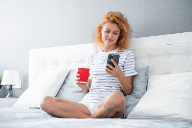 Telefonda internette kahve sörfü yapan mutlu bir kız. Kız evde telefonuyla internette sörf yapıyor. Kızın evinde internet sörfü.