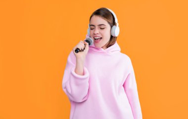 Sarı arka planda mikrofonu olan kulaklıklı mutlu genç kız şarkıcı..