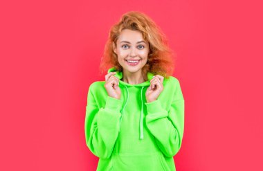 cheerful stylish woman at studio. photo of stylish woman in hoodie. redhead stylish woman on color background. stylish woman isolated on red background.