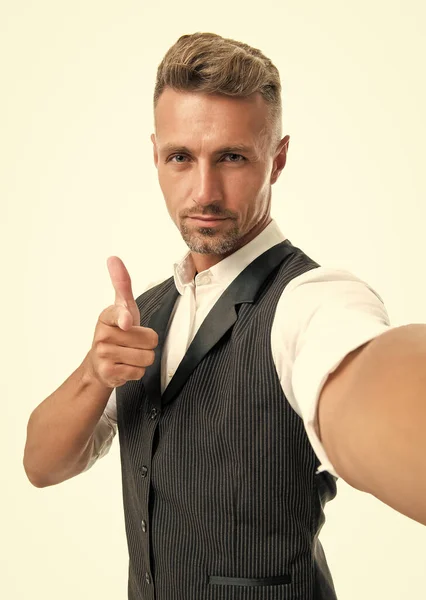 Serious manager in suit vest taking selfie pointing finger gun hand gesture isolated on white.
