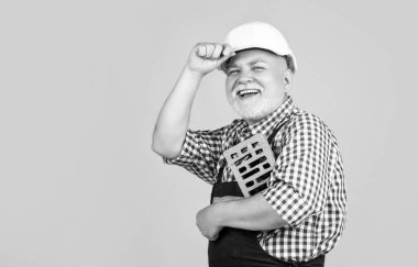 Sarı arka planda sert şapkalı, sırıtan kıdemli bir duvarcı..