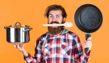 Aç adam. Kareli gömlekli profesyonel aşçı. Sakallı koca. Restoranda. İsimsiz dökme demir pişirme kabı. Yapışkan olmayan kaplamalı politetrafluoretilen teflon. Sağlıklı yemek pişirmek..