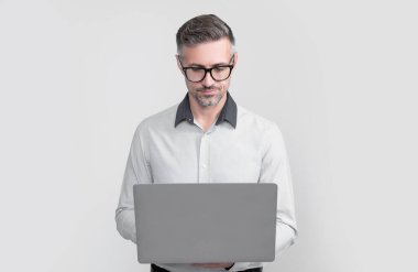 Gözlüklü olgun bir ofis çalışanı gri arka planda bilgisayar üzerinde çalışıyor..