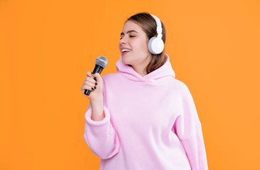 Kulaklıklı mutlu genç kız sarı arka planda mikrofonla şarkı söylüyor..