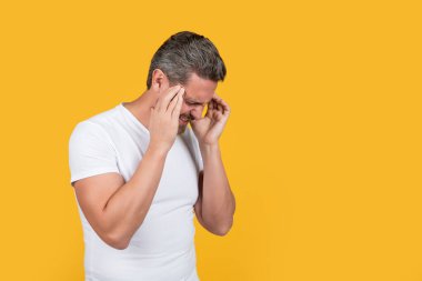 stressed man in shirt has migraine isolated on yellow with copy space. stressed man with migraine in studio. photo of caucasian stressed man with migraine wear shirt. stressed man having migraine.