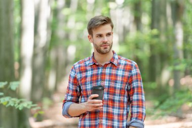 caucasian man holding coffee. caucasian man with coffee wearing checkered shirt. photo of caucasian man with coffee in the forest. caucasian man with coffee outdoor.