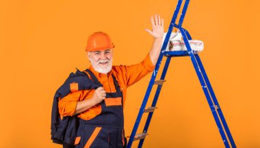 Tamir için aletler. Kıdemli boyacı merdivende paten kullanır. Duvarı sarıya boyamak. İş kıyafetleri içinde profesyonel bir ressam. Odada duvar boyama işçisi. Tekerlekli erkek dekoratör.