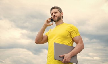 man with computer talking on smartphone on sky background.