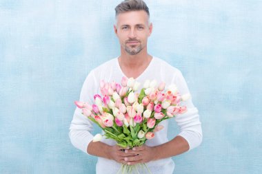man with spring tulips smile isolated on blue background. photo of man with spring tulips. man with spring tulips. man with spring tulips in studio.