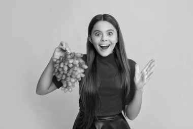 Şaşırmış çocuk sarı arka planda taze üzüm tutuyor..