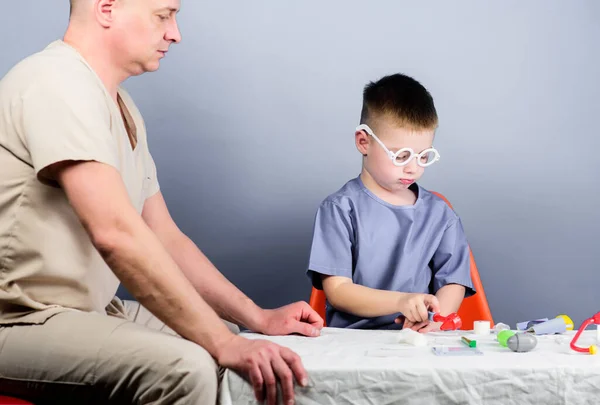 Illness treatment. Dad and son medical dynasty. Medical examination. Boy cute child and his father doctor. Hospital worker. Health care. Medicine concept. Kid little doctor sit table medical tools.