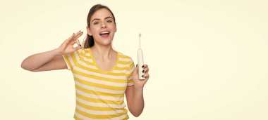 Beyaz arka planda elektrikli diş fırçası olan neşeli genç bir kadın. Tamam.