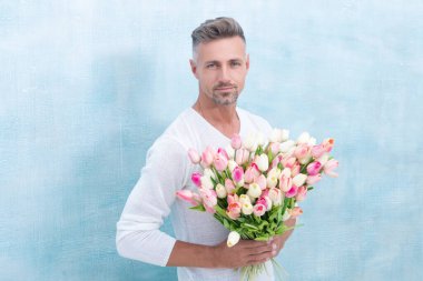photo of man holding spring tulips. man with spring tulips. man with spring tulips in studio. man with spring tulips isolated on blue background.